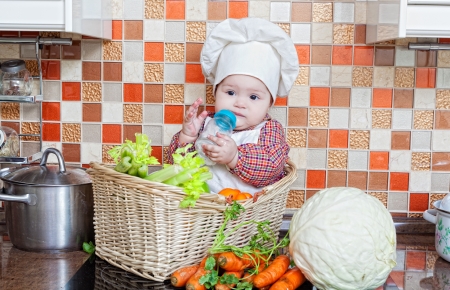 baby cook with vegetables sits in a wattled basket on a kitchen tableの写真素材
