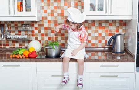 Baby cook with vegetables sits on a kitchen tableの写真素材