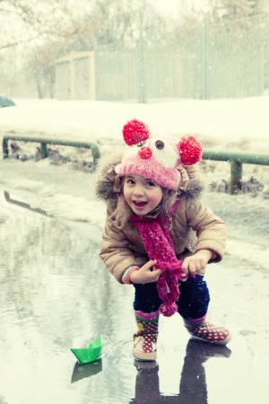 little girl plays with paper ships in a spring puddleの写真素材