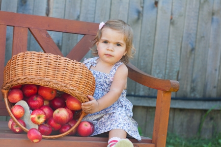 Little girl in a summer dress sits on a wooden shop with applesの写真素材
