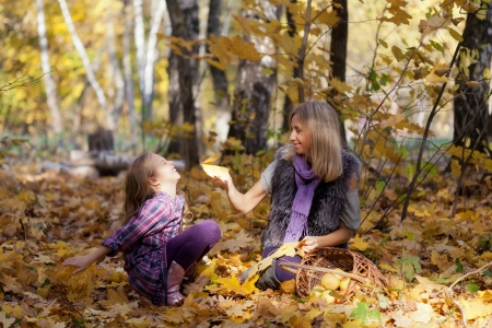Happy mum and the daughter play autumn park on the fallen down foliageの写真素材