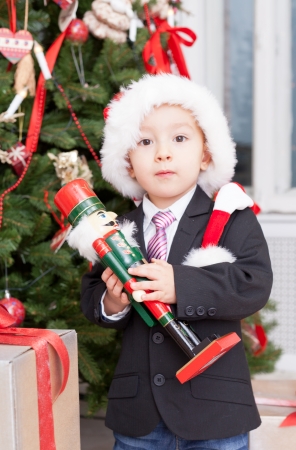  boy stands near Christmas a fir-tree with the wooden nutcracker in handsの写真素材