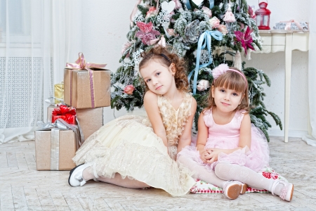 Two girls sit  near a Christmas fir-treeの写真素材