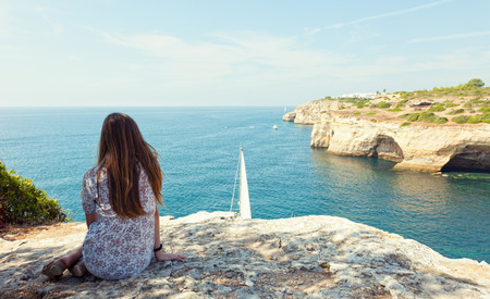 girl sits on the rock and looks at yachts at the oceanの写真素材