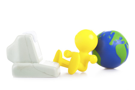  yellow little man sits near the computer, leaning a back on the Globeの写真素材