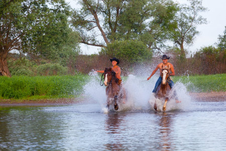 Young people skip astride horses through the riverの写真素材