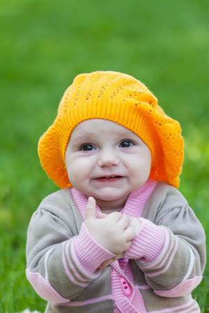 Little girl in an orange beret against a green grassの写真素材