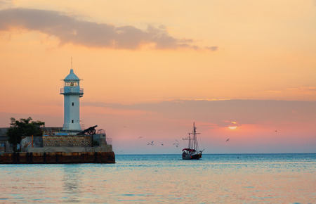 Seagulls fly round masts of the sailing ship coming into a bay on a sunsetの写真素材