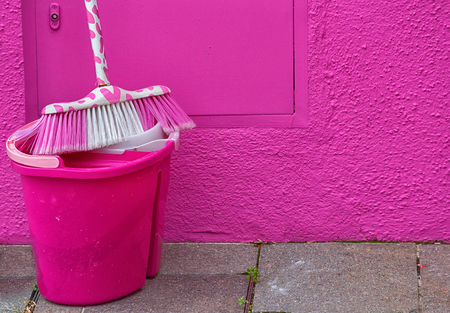 Pink bucket and a mop standing near a pink wall, close-upの写真素材