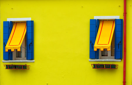 Two windows with blue shutters and awnings on the yellow wall, Burano, Veniceの写真素材