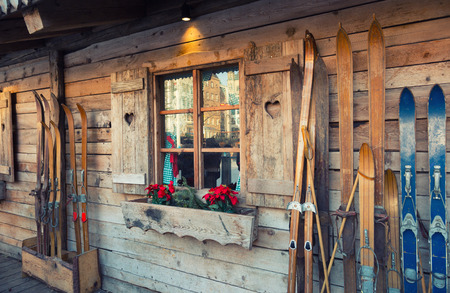 Wooden skis stand near the wall of an old house with a window, which blooms puansetiyaの写真素材