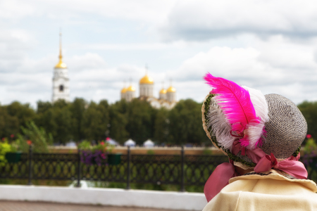 A girl in an old hat with a feather looks at the Assumption Cathedral in Vladimir, Russiaの写真素材