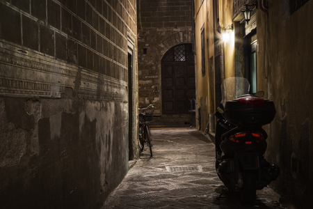 Motorcycle and bicycle stand in a dark alley at night, Florence, Italyの写真素材