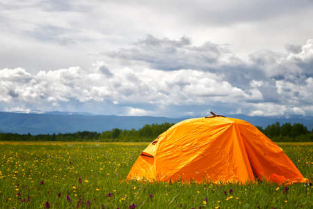Orange Tourist tent stands on the grass mountains backgroundの写真素材