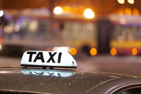 Shining Taxi inscription close up against passing cars on night street of big citの写真素材