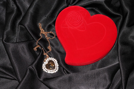 Red heart-shaped jewelry box with pendan on a black silkの写真素材