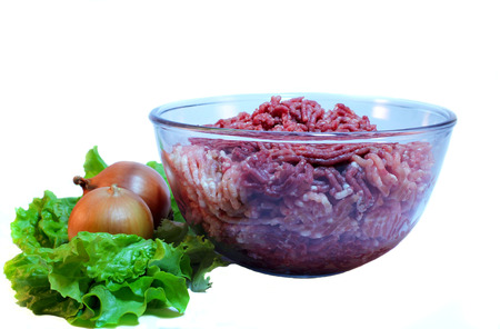 Raw minced meat in a glass bowl with lettuce and two onionsの写真素材