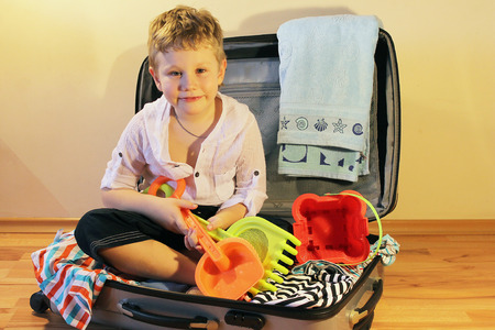 Boy sits in a suitcase with beach towels and kids sand setの写真素材