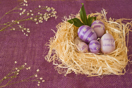 Egg with violet flowers and an inscription Happy Easter lying on the straw in the background a sackingの写真素材