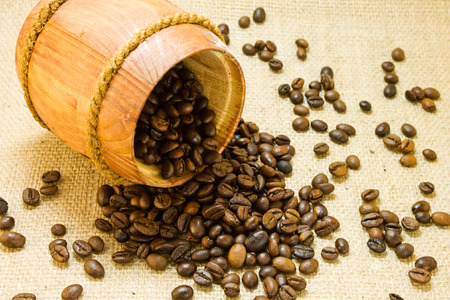 Coffee beans spilled from a lying wooden jar on the background of a sackingの写真素材