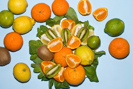 Lemons, tangerines, kiwi and lime stacked on a plate with mint leaves top viewの写真素材