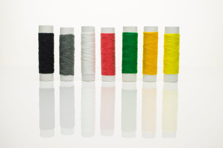 Threads for sewing different colors stacked in a row on a white isolated background with reflection