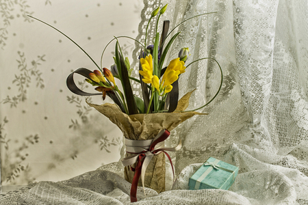 Flowers in a vase and a gift box of blue color on the background of lace in retro styleの写真素材