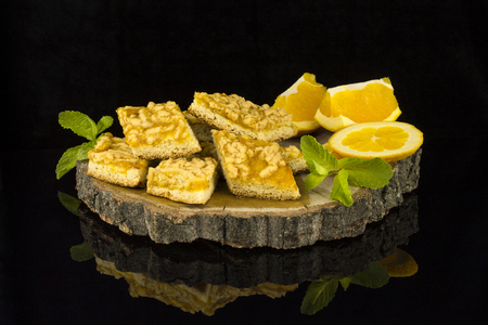 Cookies with marmalade decorated with mint leaves and orange slices on a tree stump on a black background with reflectionの写真素材