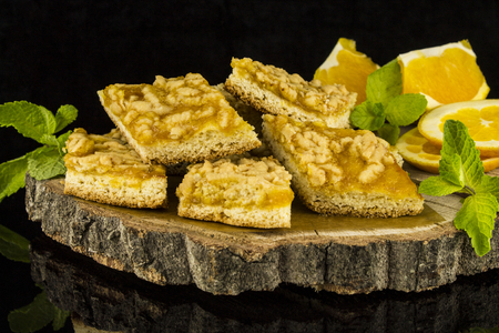 Cookies with marmalade decorated with mint leaves and orange slices on a tree stump on a black background with reflectionの写真素材