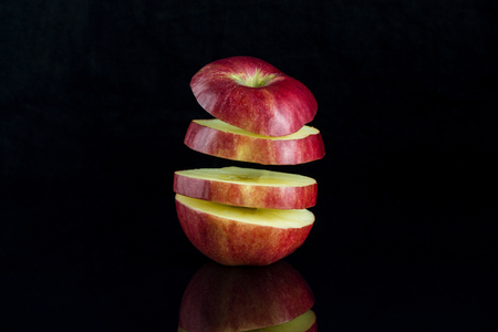 Apple cut into slices hanging in the air on a black background with reflectionの写真素材