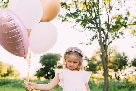Small shiny girl with pink balloons in the gardenの写真素材