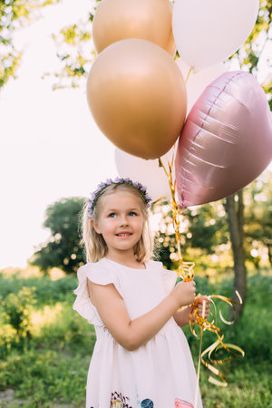 Small shiny girl with pink balloons in the gardenの写真素材