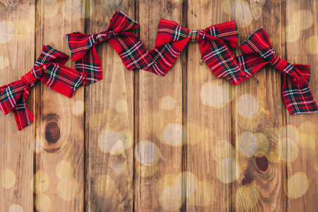 Christmas red bows on brown wooden background with lights bokehの写真素材