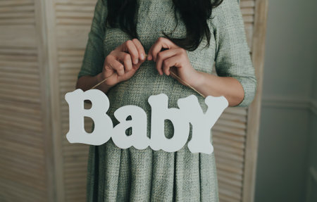 Pregnant woman holding wooden word baby. Waiting for a babyの写真素材