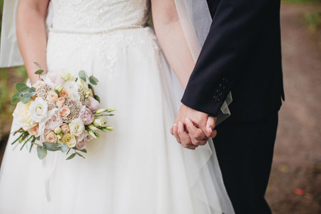 Bride in white dress is holding wedding bouquet. Groom hugs brideの写真素材
