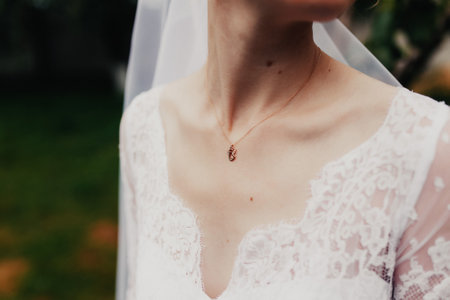 Gold pendant around the neck of the bride in a white dress with veilの写真素材