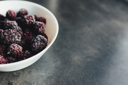 Frozen blackberries in a bowl on the table. Blurred backgroundの写真素材