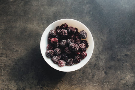 Frozen blackberries in a bowl on the table. Blurred background