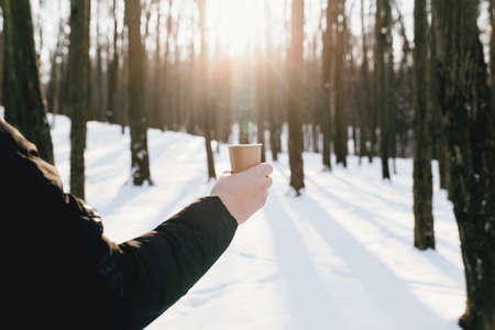 The guy holds a paper cup of coffee in his hand in the snowy forestの写真素材