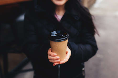 Girl holds a paper cup of coffee in hand near cafeの写真素材