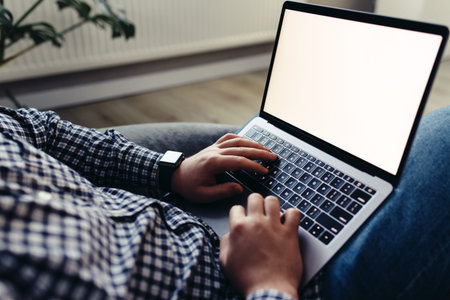 Man using laptop, wearing glasses, cushioned furniture. Blurred background