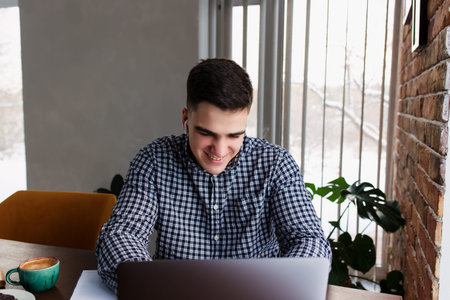 Smiling man working at laptop with a cup of coffee at home. Blurred background. High quality photo