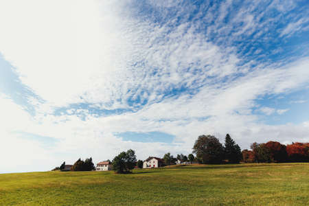 Landscape of green fields, private houses in distance, beautiful clouds in skyの写真素材