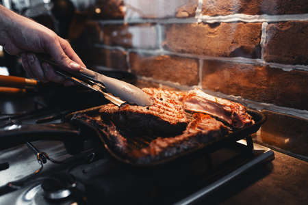 Hand turns steak with tongs during preparation on the grill pan with seasonings. High quality photoの写真素材
