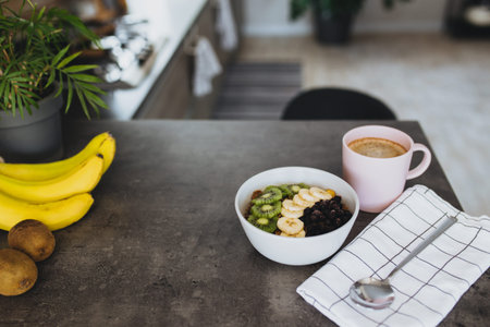 Pink coffee cup, bowl with chopped fruits and blueberries, spoon in kitchenの写真素材