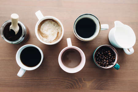Multiple coffee cups, milk, beans and ground coffee in jar on wooden backgroundの写真素材