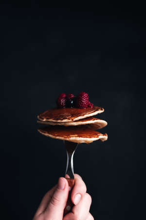 Hand holds a fork with juicy pancakes with berries and honey. High quality photoの写真素材