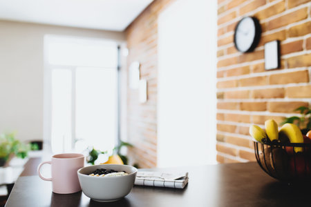 Pink coffee cup, bowl with chopped tropical fruits kiwi and banana, blueberries, spoon on bar counter in stylish loft kitchen. Blurred background. High quality photoの写真素材