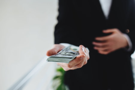 One hundred dollar bills money bundle, in hand of man in suit and white shirt. Blurred background. High quality photoの写真素材