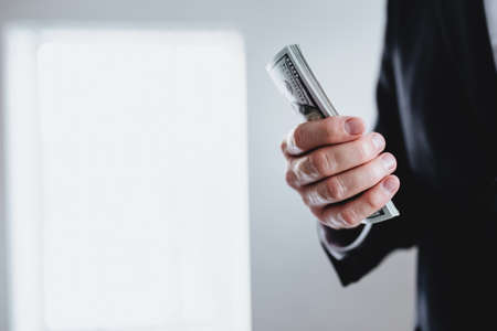One hundred dollar bills money bundle, in hand of man in suit and white shirt. Blurred background. High quality photoの写真素材